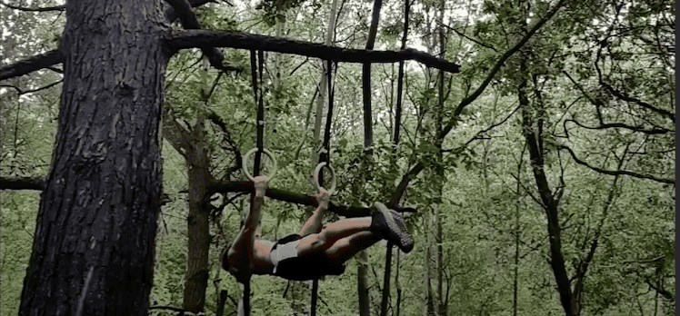 omme faisant un back lever dans la forêt grâce à des anneaux : l'indispensable du matériel street workout